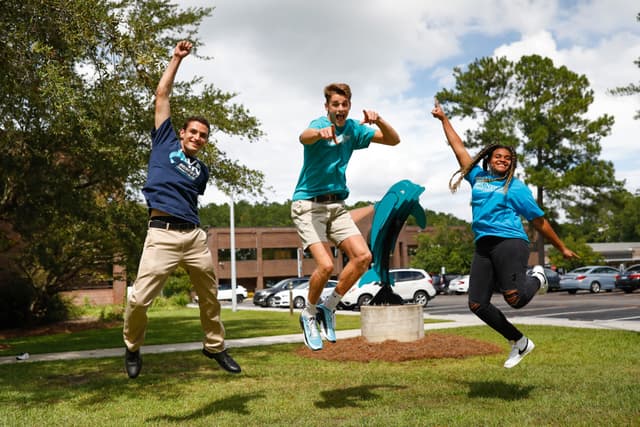 two young men and a young woman jump into the air