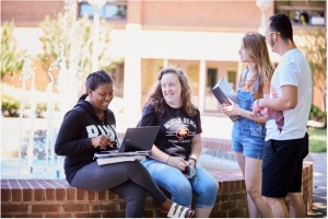 students sitting outside on campus with laptops